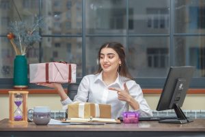 Adorable girl holding gift box and pint finger on it at office