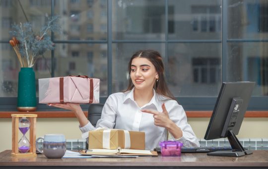 Adorable girl holding gift box and pint finger on it at office